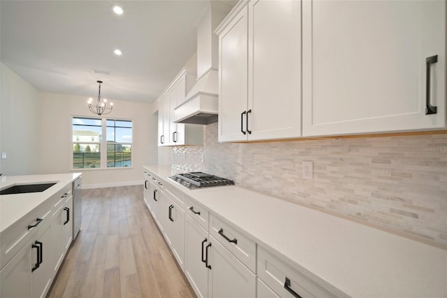 kitchen featuring light wood-style flooring, tasteful backsplash, a notable chandelier, custom range hood, and appliances with stainless steel finishes