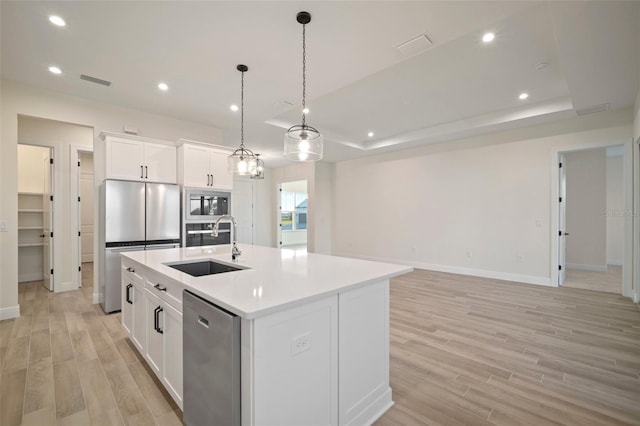 kitchen with light wood-type flooring, stainless steel appliances, a kitchen island with sink, and a sink