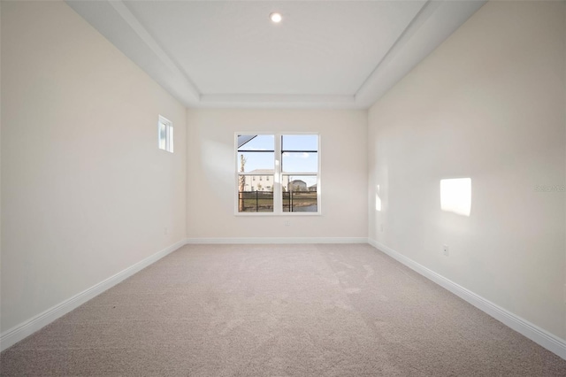 spare room featuring a raised ceiling, light carpet, and baseboards