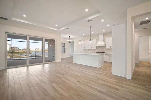 kitchen featuring open floor plan, custom range hood, baseboards, visible vents, and a raised ceiling