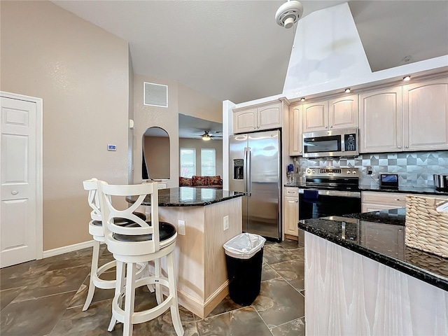 kitchen featuring ceiling fan, decorative backsplash, appliances with stainless steel finishes, and dark stone countertops