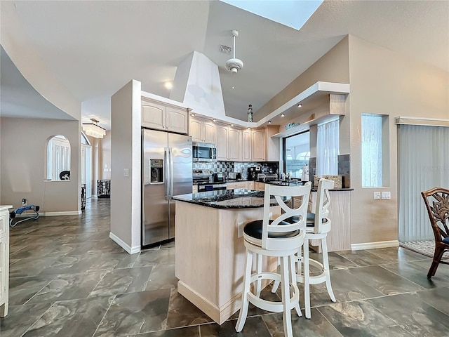 kitchen featuring decorative backsplash, appliances with stainless steel finishes, a kitchen breakfast bar, high vaulted ceiling, and dark stone counters