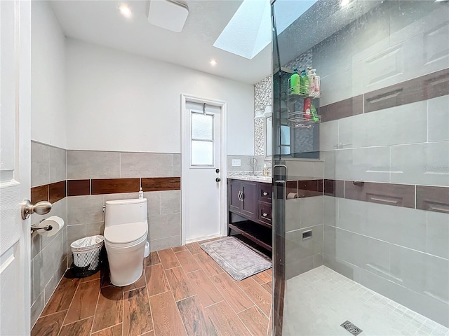 bathroom featuring toilet, vanity, tile walls, walk in shower, and a skylight