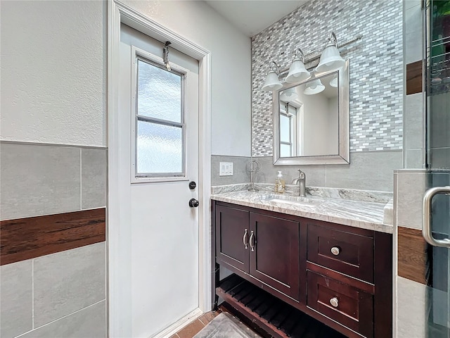 bathroom featuring a shower with shower door, vanity, backsplash, and tile walls