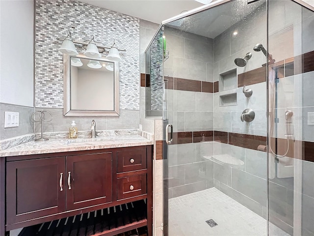 bathroom with a shower with shower door, tile walls, vanity, and tasteful backsplash