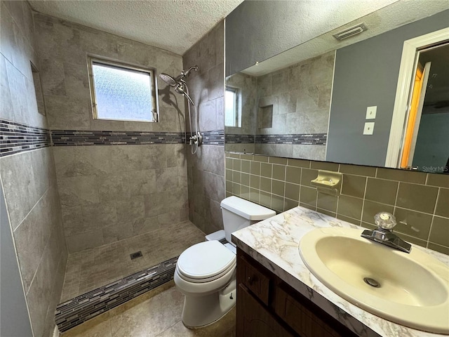 bathroom with a tile shower, backsplash, a textured ceiling, toilet, and vanity