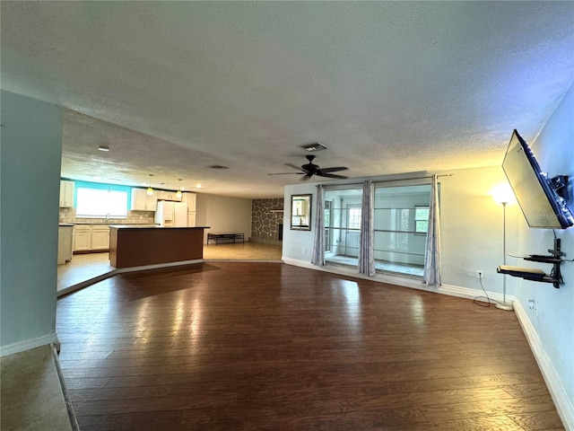 unfurnished living room with ceiling fan, a textured ceiling, and dark hardwood / wood-style flooring