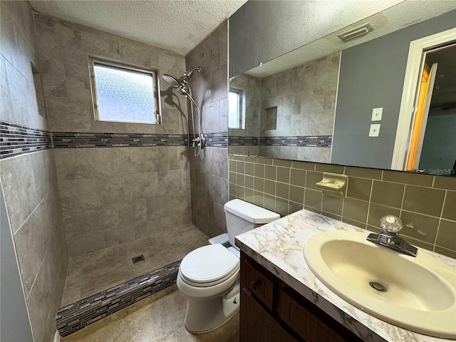 bathroom featuring a textured ceiling, vanity, tasteful backsplash, toilet, and tiled shower