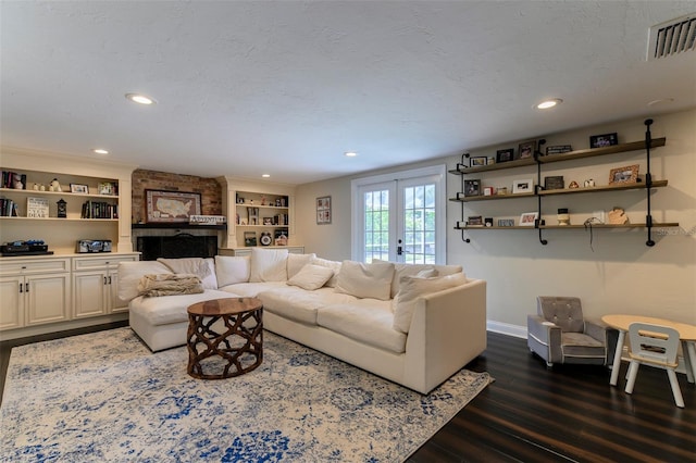 living room with a textured ceiling, dark wood-type flooring, built in features, and french doors