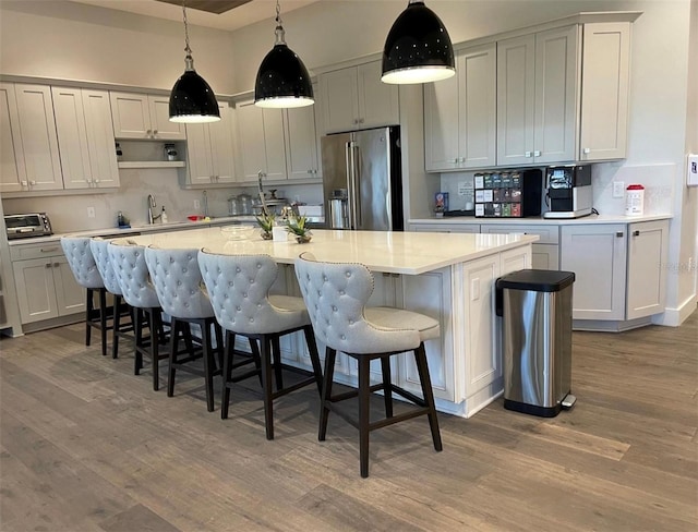 kitchen featuring a center island with sink, wood-type flooring, a breakfast bar area, and high end fridge