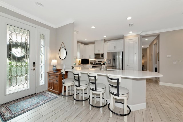 kitchen with a breakfast bar, white cabinetry, stainless steel appliances, ornamental molding, and kitchen peninsula