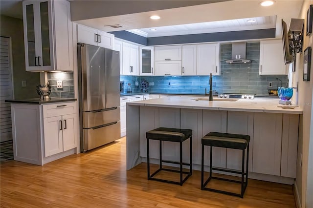 kitchen featuring white cabinetry, tasteful backsplash, light hardwood / wood-style flooring, stainless steel refrigerator, and wall chimney range hood