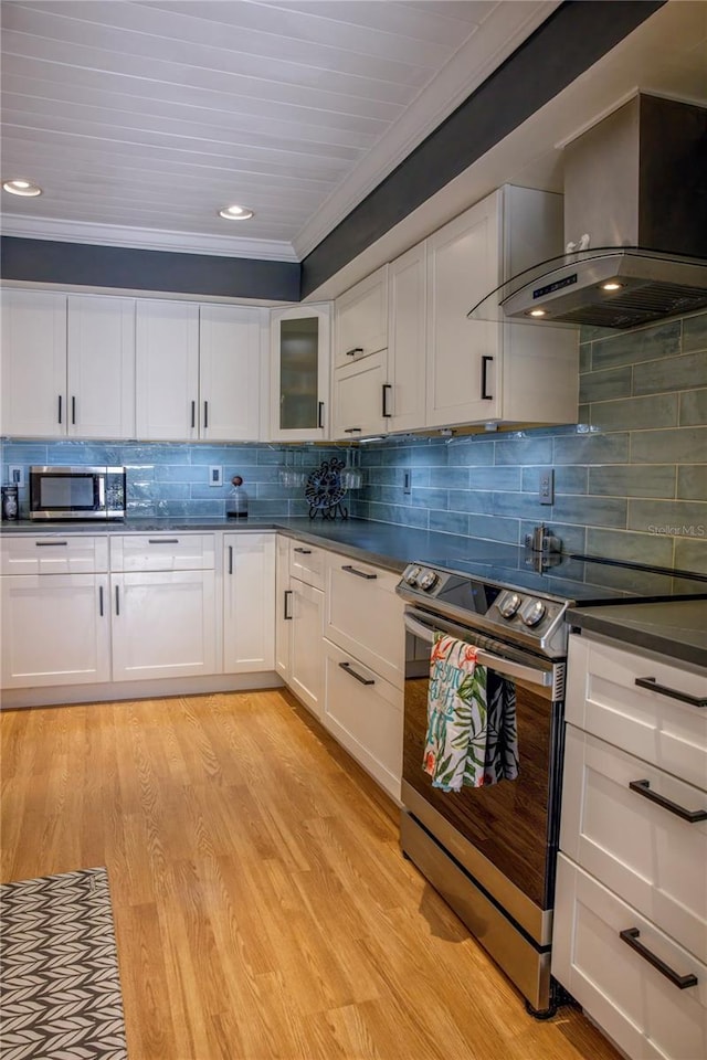 kitchen with white cabinetry, wall chimney range hood, light hardwood / wood-style floors, and appliances with stainless steel finishes