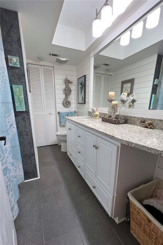 bathroom with vanity, tile patterned floors, toilet, and wood walls