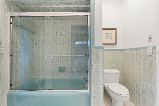 bathroom featuring toilet, tile patterned floors, bath / shower combo with glass door, and tile walls