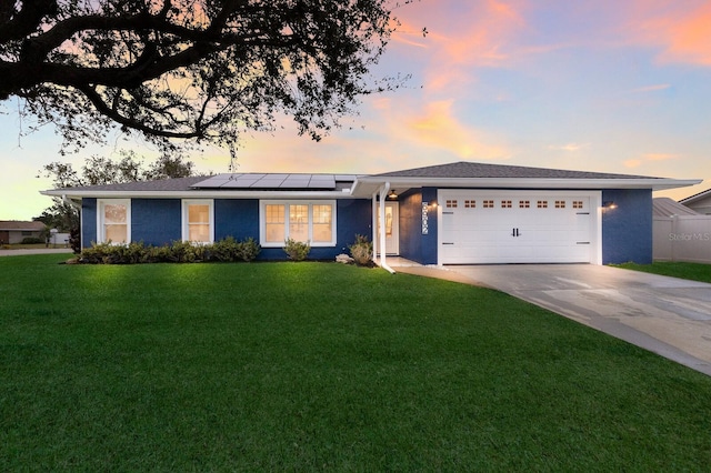 ranch-style house with a garage, a lawn, and solar panels