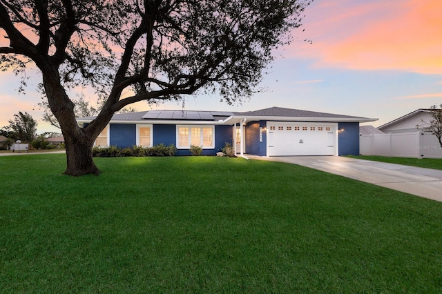 ranch-style house featuring a garage, a lawn, and solar panels