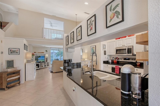 kitchen with white cabinets, appliances with stainless steel finishes, a towering ceiling, sink, and light tile patterned floors