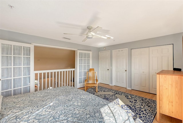 bedroom with wood-type flooring, two closets, and ceiling fan