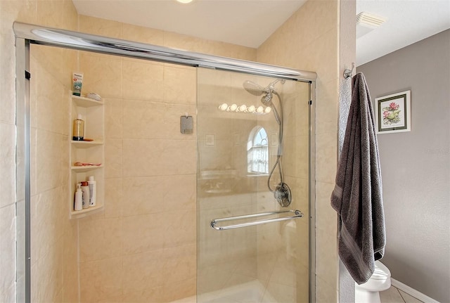 bathroom featuring a shower with door and toilet