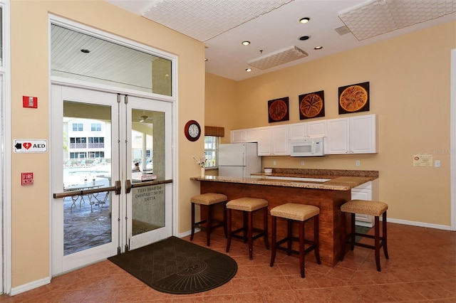 kitchen with white appliances, white cabinetry, french doors, a kitchen breakfast bar, and kitchen peninsula