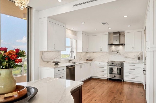 3060 Grand Bay Blvd Unit 175, Longboat Key, FL 34228 - kitchen with wall chimney range hood, stainless steel appliances, a sink, white cabinetry, and hardwood / wood-style floors