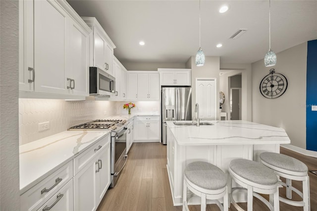 kitchen with decorative light fixtures, white cabinetry, stainless steel appliances, and a kitchen island with sink