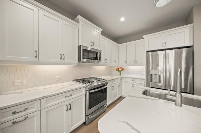 kitchen featuring appliances with stainless steel finishes, backsplash, white cabinets, and light stone countertops