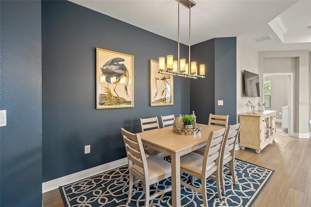 dining area with light wood-type flooring, an inviting chandelier, and ornamental molding