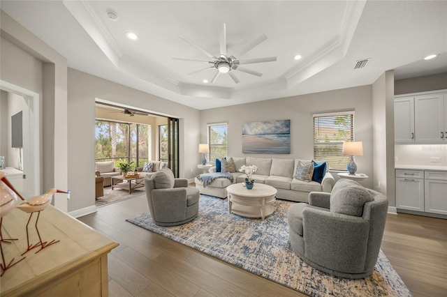 living room with hardwood / wood-style flooring, ceiling fan, ornamental molding, and a raised ceiling