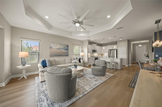 living room with sink, ornamental molding, a raised ceiling, light wood-type flooring, and ceiling fan