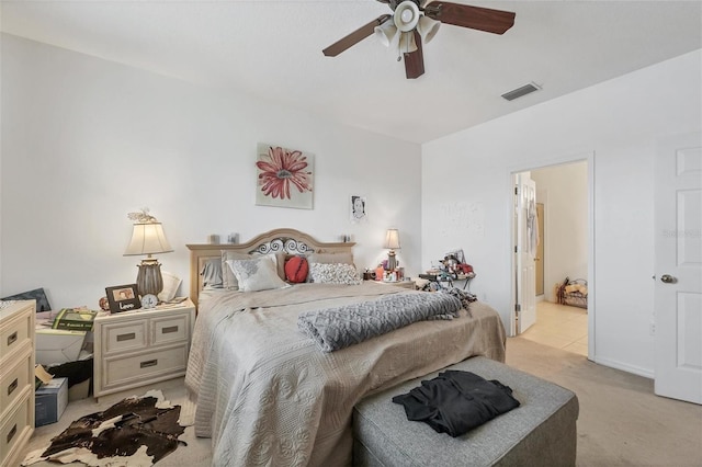 bedroom with ceiling fan, light colored carpet, and ensuite bath