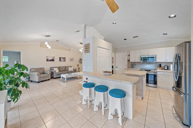 kitchen with vaulted ceiling, light tile patterned floors, decorative backsplash, white cabinets, and stainless steel appliances