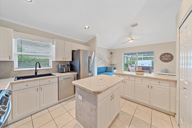 kitchen with appliances with stainless steel finishes, tile counters, a kitchen island, white cabinetry, and sink