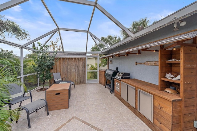 view of patio / terrace featuring glass enclosure, exterior kitchen, and a grill