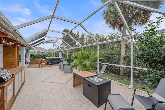 view of patio / terrace featuring glass enclosure, a hot tub, an outdoor kitchen, and a fire pit