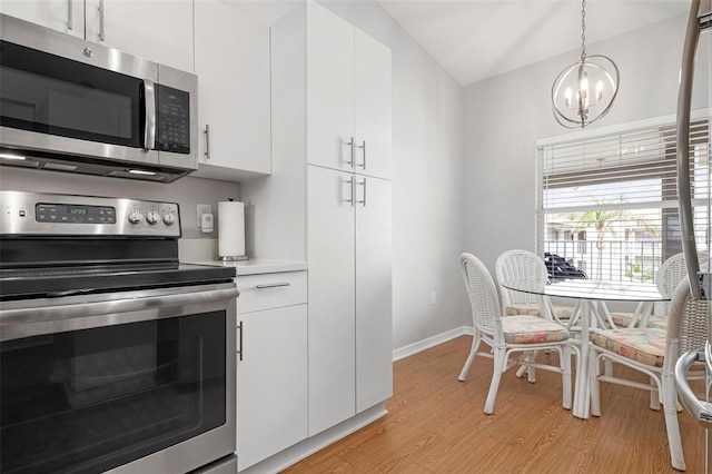 kitchen featuring white cabinetry, stainless steel appliances, hanging light fixtures, a chandelier, and light hardwood / wood-style flooring