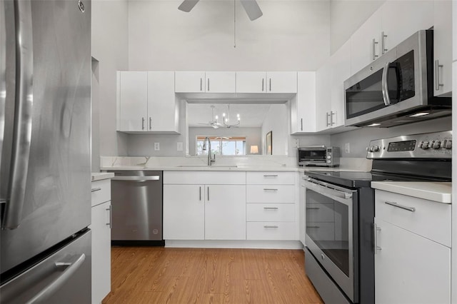 kitchen featuring appliances with stainless steel finishes, decorative light fixtures, white cabinets, light hardwood / wood-style flooring, and sink