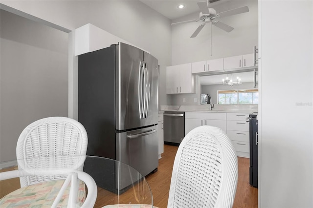 kitchen featuring ceiling fan with notable chandelier, hardwood / wood-style floors, white cabinets, appliances with stainless steel finishes, and sink