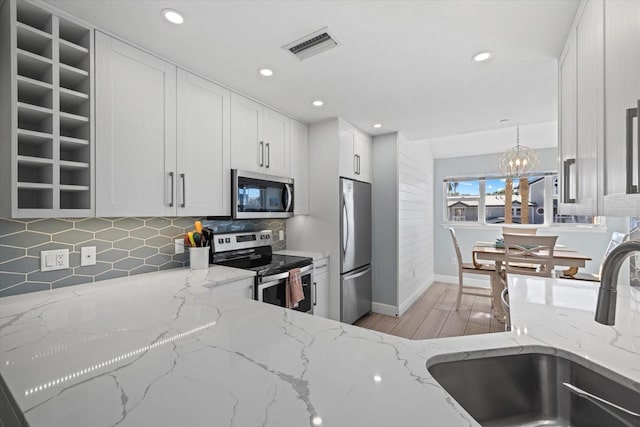 kitchen featuring light stone countertops, decorative light fixtures, white cabinetry, stainless steel appliances, and sink