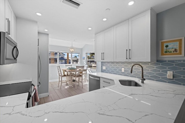 kitchen with appliances with stainless steel finishes, sink, decorative light fixtures, white cabinets, and light stone counters