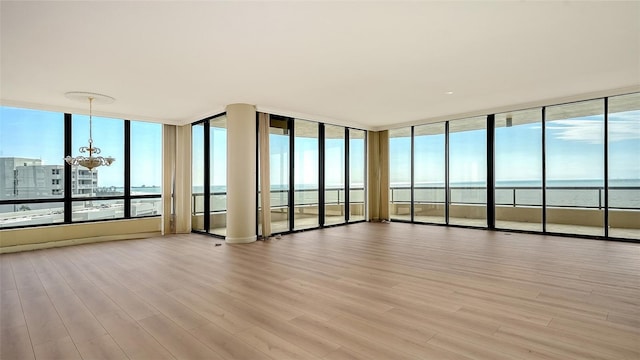 unfurnished room with an inviting chandelier, light hardwood / wood-style floors, and a water view