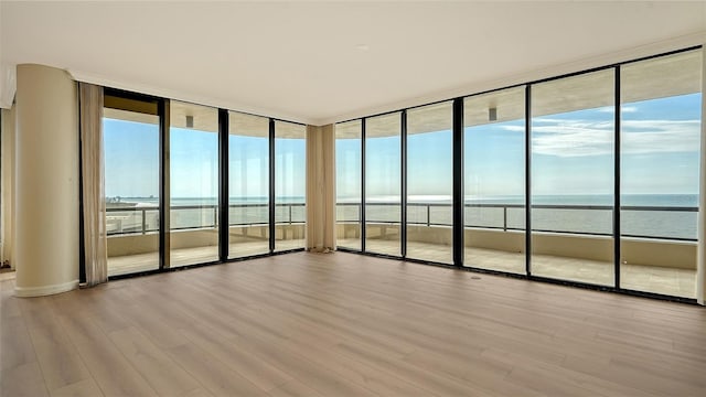 spare room featuring a water view, expansive windows, and light hardwood / wood-style floors