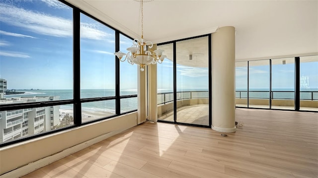 unfurnished sunroom with a water view, an inviting chandelier, and a view of the beach