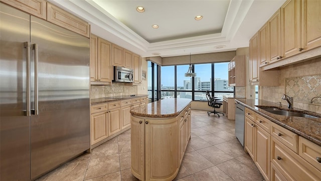 kitchen with dark stone countertops, a kitchen island, a tray ceiling, hanging light fixtures, and stainless steel appliances