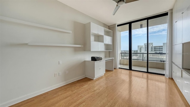 unfurnished office featuring ceiling fan, a wall of windows, and light wood-type flooring