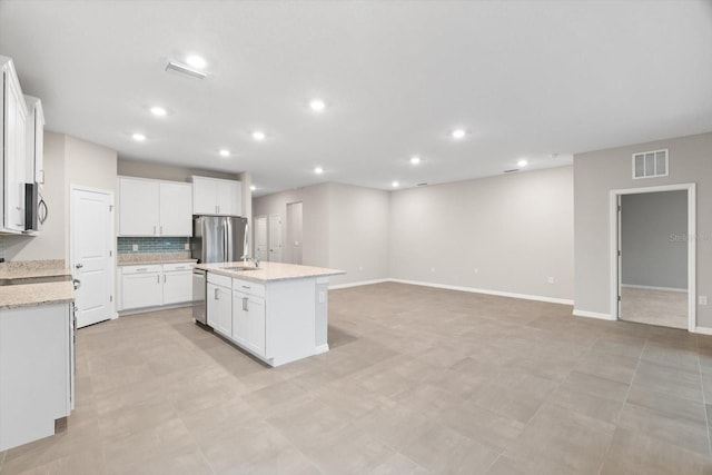 kitchen with a kitchen island with sink, light stone countertops, stainless steel appliances, and white cabinets