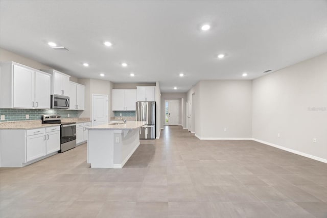 kitchen with light stone countertops, appliances with stainless steel finishes, a center island with sink, and white cabinets