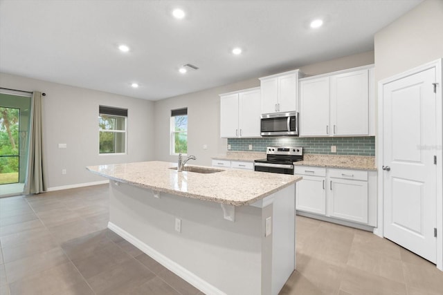 kitchen featuring sink, white cabinetry, stainless steel appliances, light stone countertops, and a center island with sink