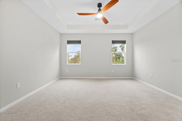 unfurnished room featuring ceiling fan, a healthy amount of sunlight, a raised ceiling, and carpet